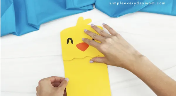 hands gluing body to chick paper bag puppet