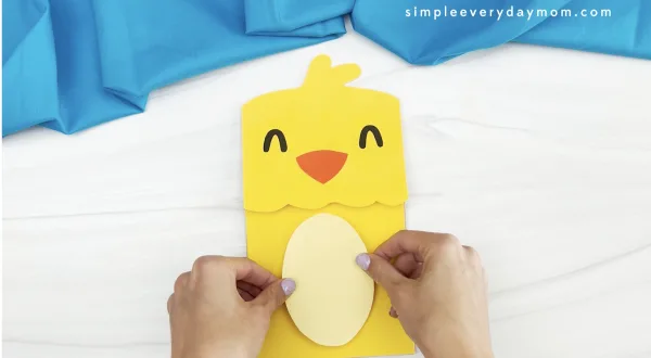 hands gluing belly to chick paper bag puppet