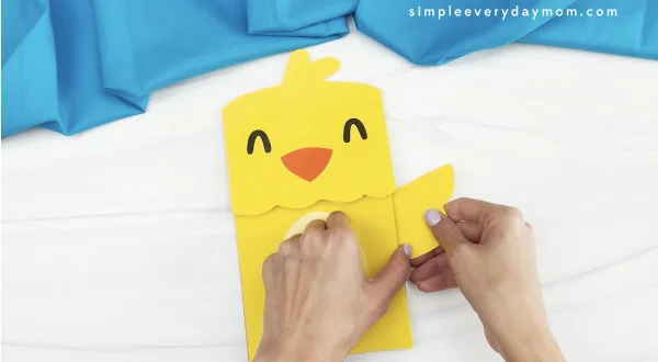 hands gluing wing to chick paper bag puppet