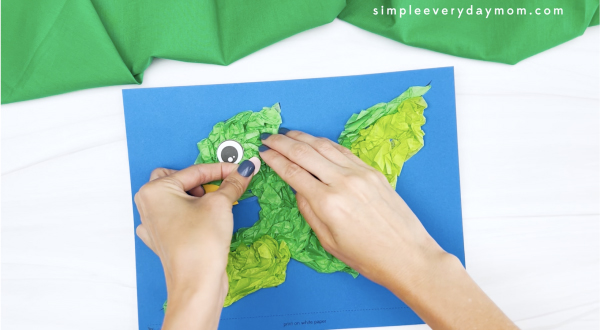hand gluing cheek to dinosaur tissue paper craft