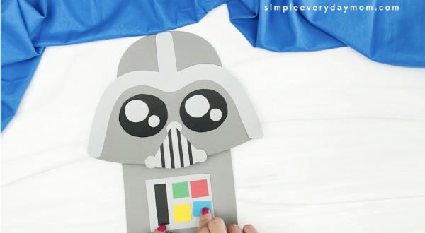 hand gluing buttons to Darth Vader paper bag puppet craft