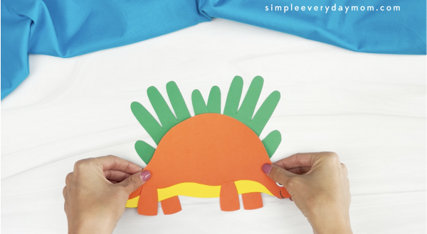hand gluing body to handprint stegosaurus