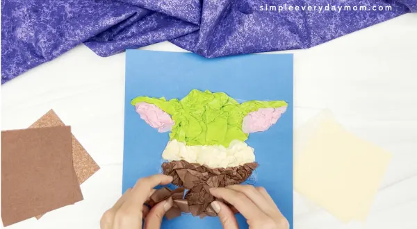 hand gluing brown tissue paper to Baby Yoda tissue paper craft