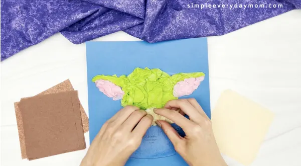 hand gluing cream tissue paper to Baby Yoda tissue paper craft