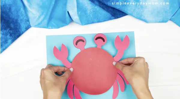 hand gluing paper crab to blue paper