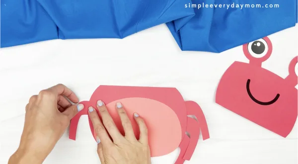 hand gluing legs to crab paper bag puppet craft