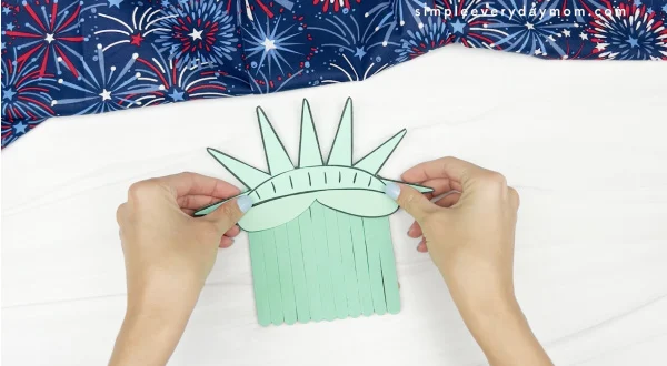 hand gluing top of Statue of Liberty to popsicle sticks