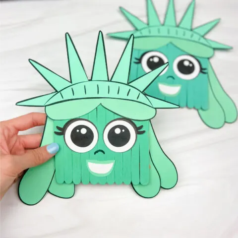 hand holding popsicle stick Statue of Liberty craft with another one in the background