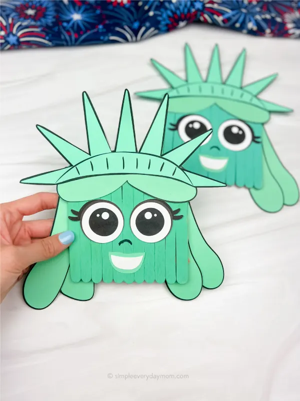 hand holding popsicle stick Statue of Liberty craft with another one in the background