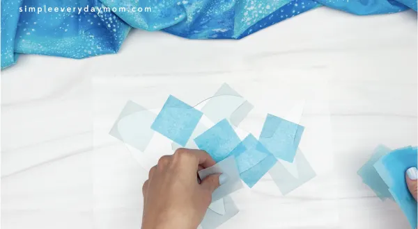 hand placing tissue paper squares on contact paper