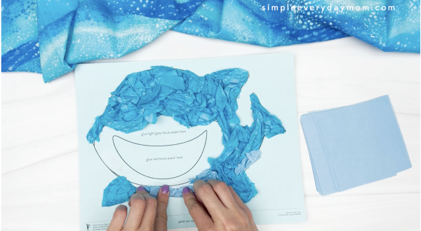 hand gluing light blue tissue paper to tissue paper shark craft