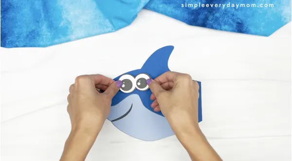 hands gluing eyes to shark handprint craft