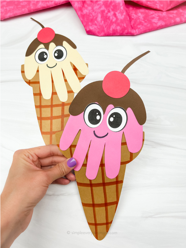 hand holding pink handprint ice cream craft with cream ice cream handprint craft in background