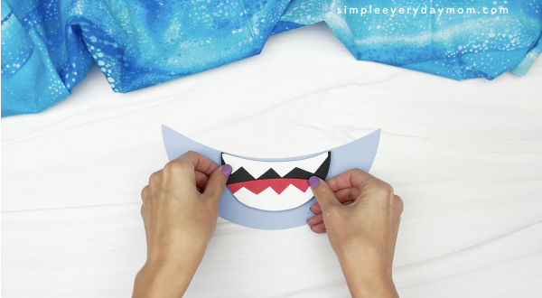 hand gluing mouth to lower face of to paper plate shark