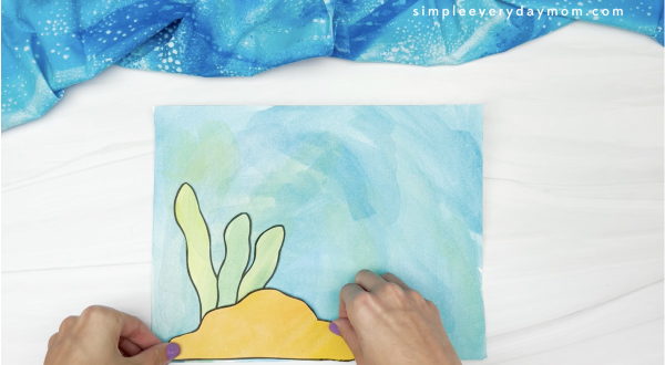 hand gluing rock to watercolor ocean scene
