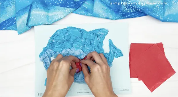 hand gluing red tissue paper to tissue paper shark craft