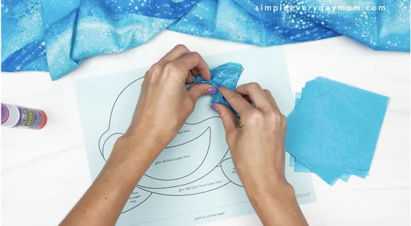 hand gluing blue tissue paper to tissue paper shark craft