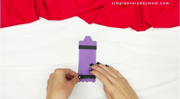 hands gluing black strip to popsicle stick crayon craft