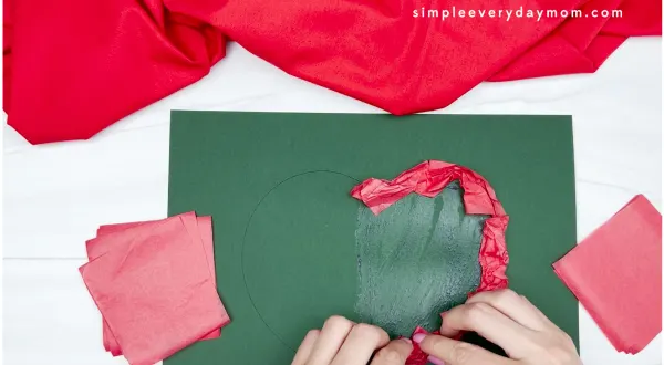 hand gluing red tissue paper on dark green paper