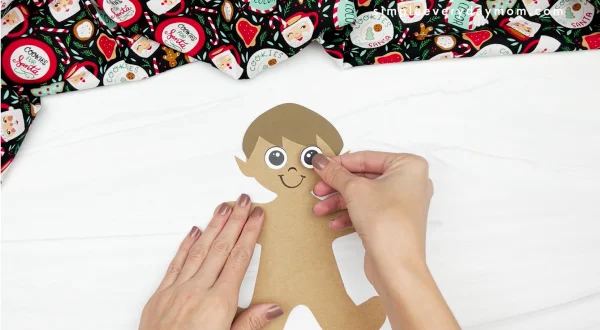 hand gluing eye to elf gingerbread man in disguise craft