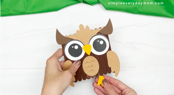 hands gluing feet to owl popsicle stick craft