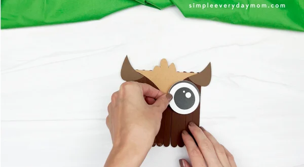 hands gluing eye to owl popsicle stick craft