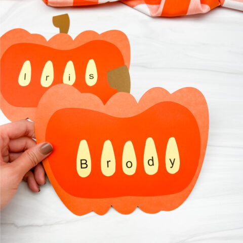 hand holding pumpkin name craft with another one in the background