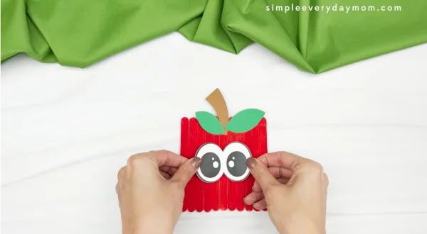 hand gluing eye onto apple popsicle stick craft