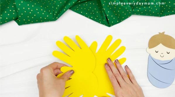 hands gluing yellow handprints together to form hay for handprint manger craft
