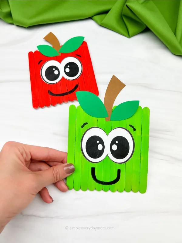 hand holding apple popsicle stick craft with another one in the background