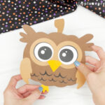 hands gluing feet to owl pumpkin craft
