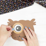 hands gluing eye to owl pumpkin craft