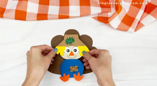 hands gluing feathers to scarecrow turkey disguise craft