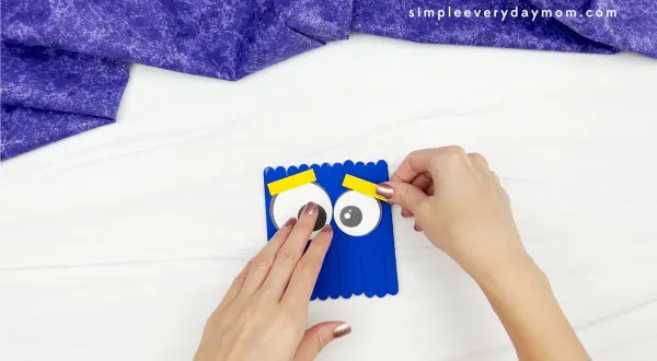 hand gluing eyebrow to monster popsicle stick craft