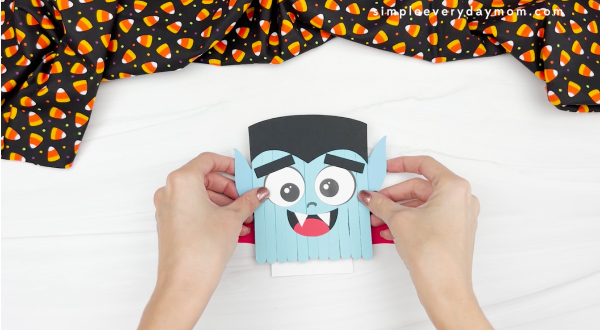 hands gluing cape to vampire popsicle stick craft