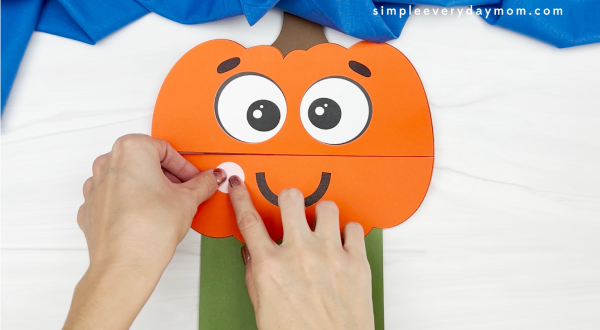 hand gluing cheek to pumpkin paper bag craft