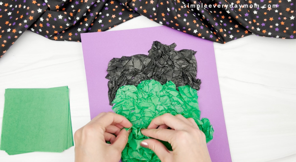 hand gluing green tissue paper to Frankenstein background