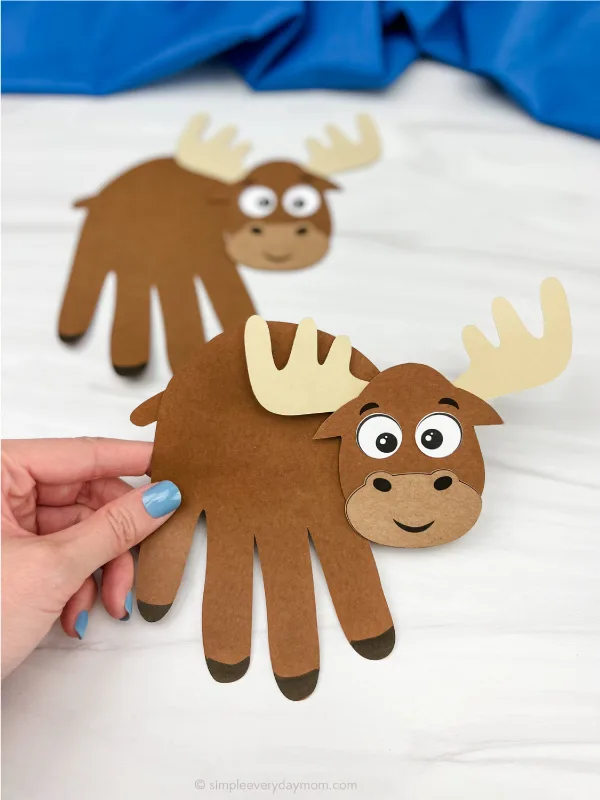 hand holding moose handprint craft with a second one in the background