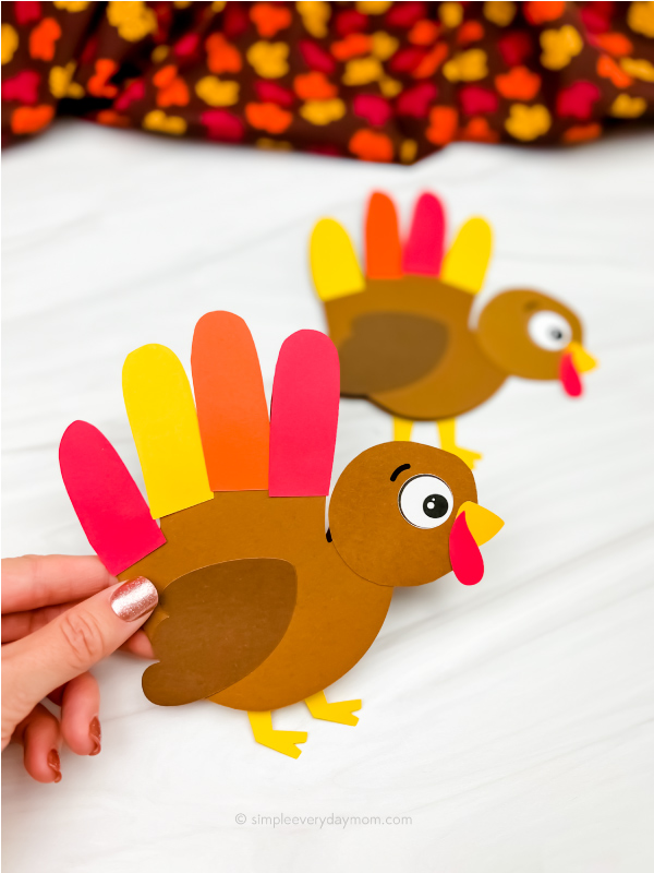 hand holding turkey handprint card craft with a 2nd one in the background