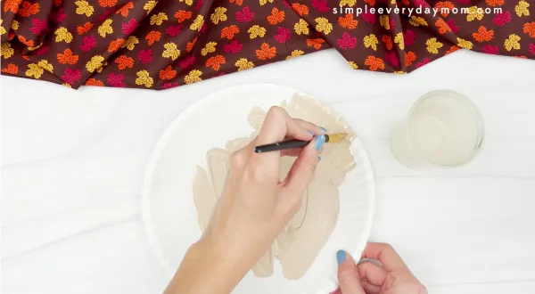 hands painting paper plate tan