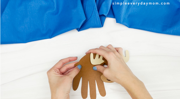 hands gluing tail to moose handprint craft