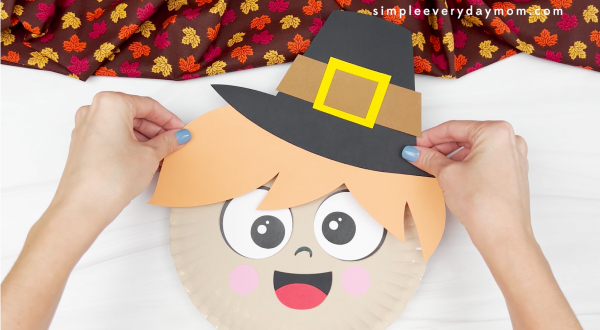hands gluing hair and hat to paper plate pilgrim craft