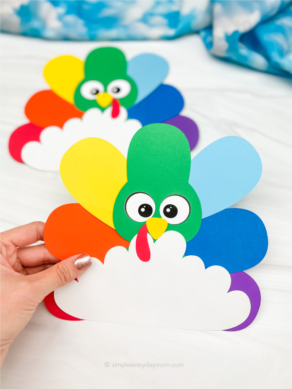 hand holding rainbow disguise a turkey craft with a 2nd one in the background