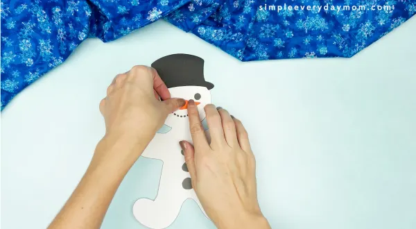 hand gluing nose onto snowman gingerbread man disguise craft