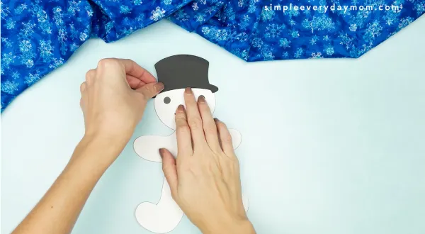 hand gluing hat onto snowman gingerbread man disguise craft
