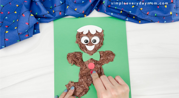 hands gluing button decoration to tissue paper gingerbread man craft