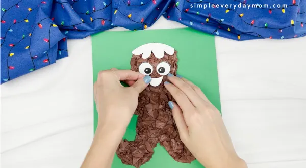 hands gluing mouth decoration to tissue paper gingerbread man craft