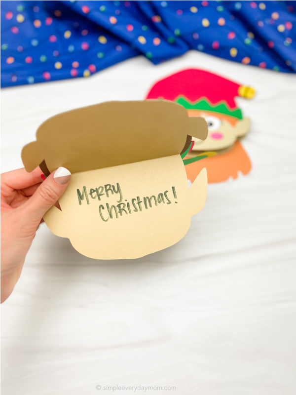 hand holding open boy elf Christmas card craft with a girl one in the background
