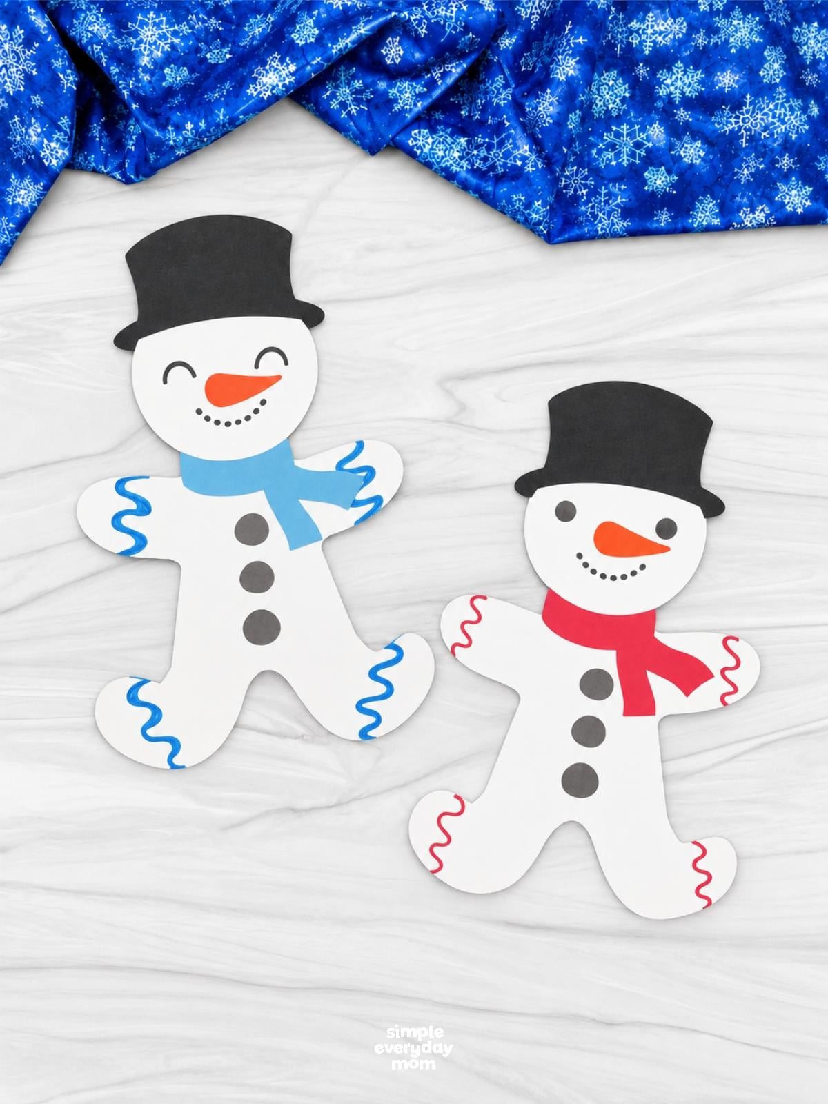 Two completed snowman gingerbread crafts with red and blue scarves, black top hats, and orange carrot noses.