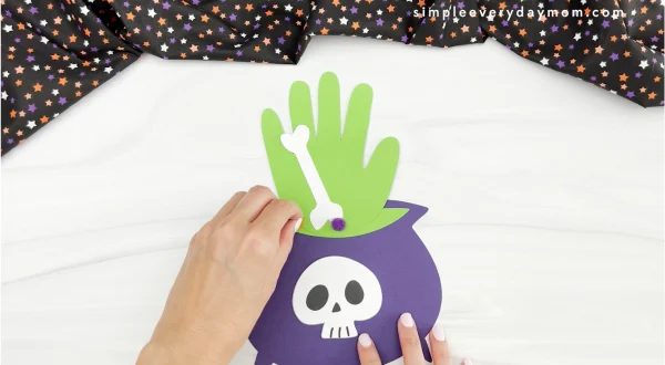 hands gluing pom pom to witches brew handprint craft